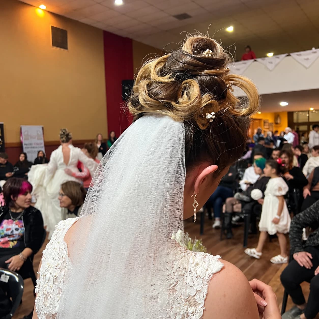 Peinado recogido con velo y vestido de encaje, fotografiado en un evento.