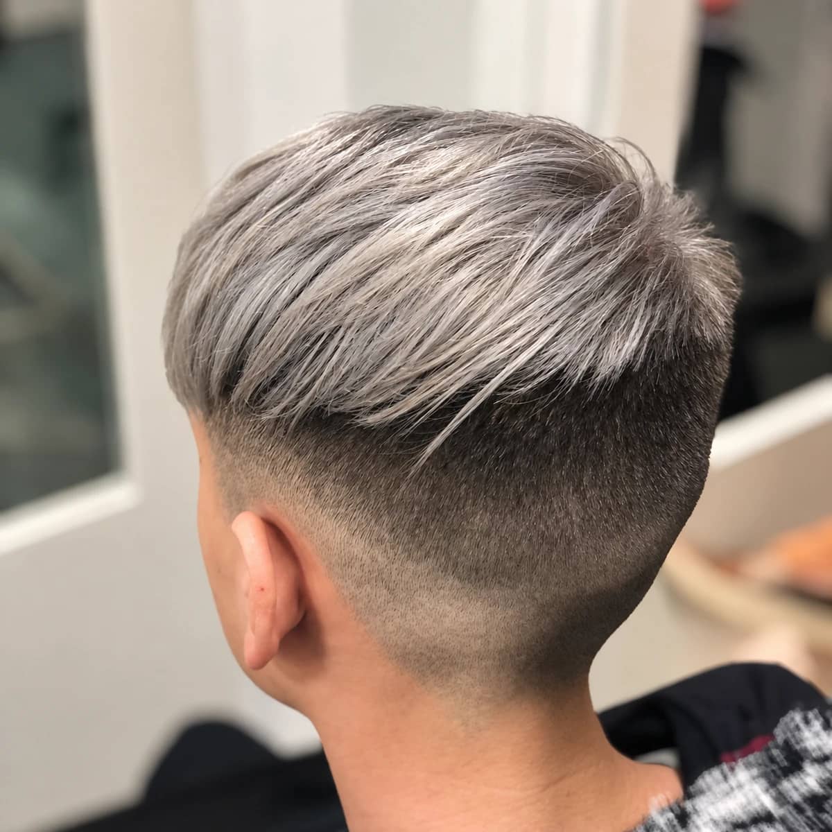 Corte corto con degradado y cabello plateado peinado hacia un lado.